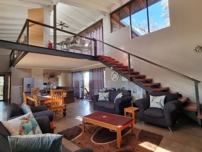 Spacious open-plan living area featuring a mezzanine level, exposed beam ceilings, concrete floors, and a modern steel staircase connecting the levels.