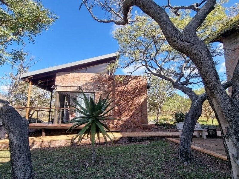A rear view of a modern home featuring exposed brick walls, a timber deck, and large sliding glass doors set within a natural garden.