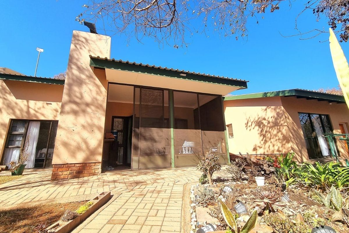 Rear view of the house featuring a covered patio area with brick paving, sliding glass doors, and a prominent brick chimney.