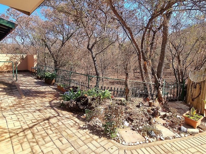 A spacious outdoor patio area featuring paved flooring and metal railings, overlooking a natural wooded landscape.