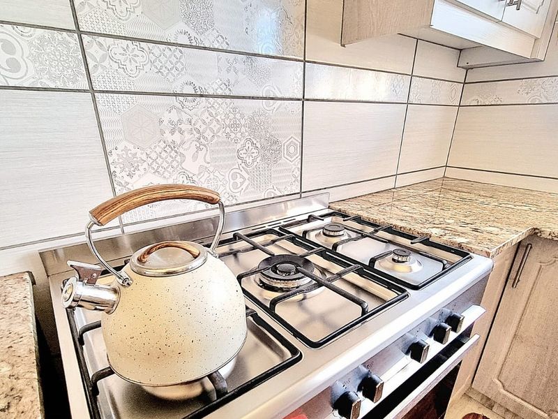 A well-maintained kitchen area featuring a gas hob, built-in oven, granite countertops, and decorative patterned tile backsplash.