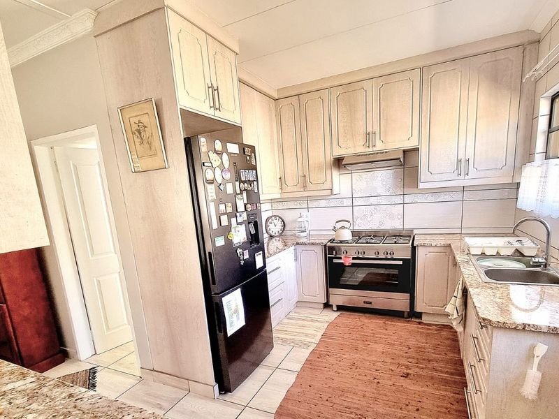 A functional kitchen featuring light-toned cabinetry, granite countertops, a stainless steel gas stove with extractor fan, and a double basin sink.