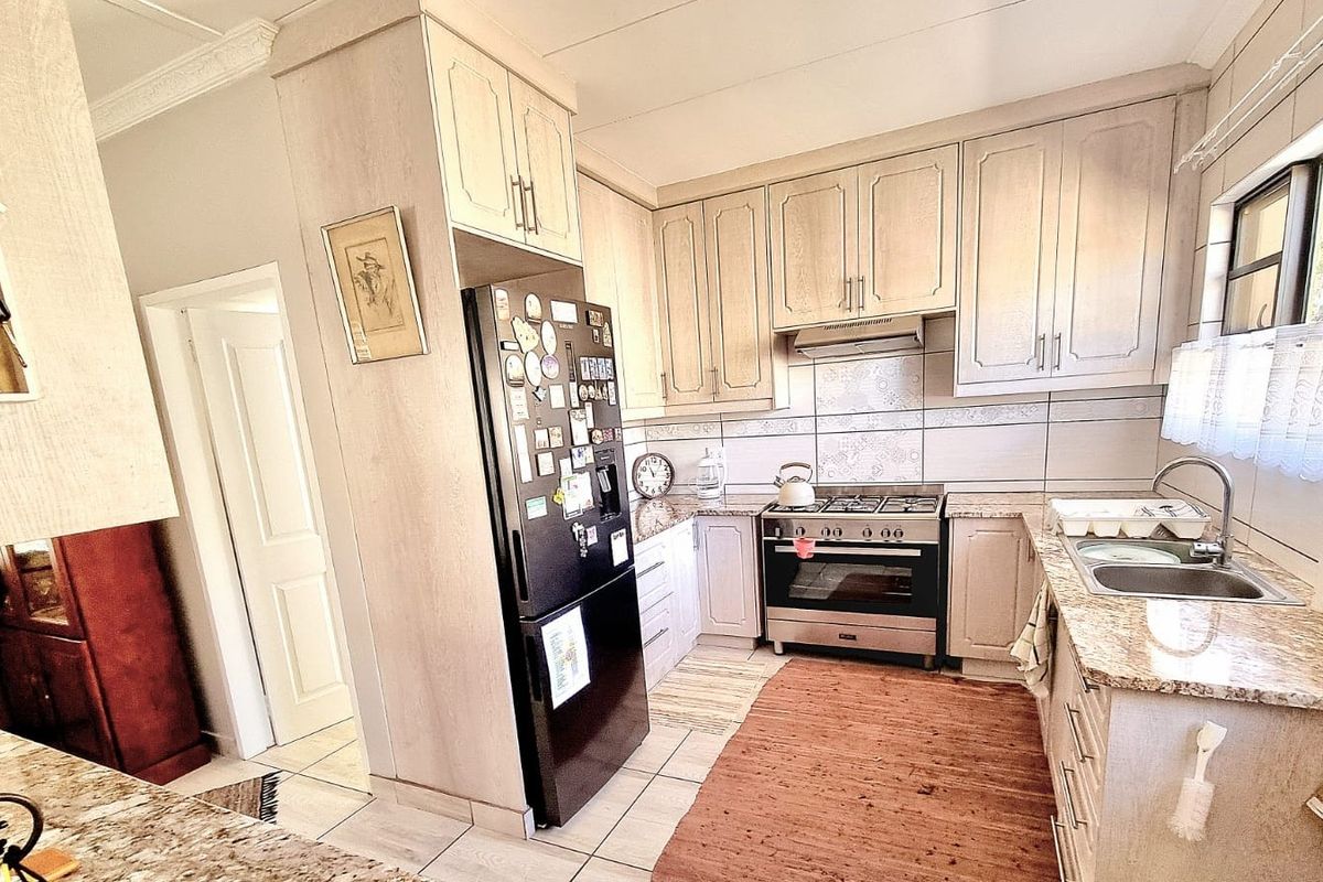 A functional kitchen featuring light-toned cabinetry, granite countertops, a stainless steel gas stove with extractor fan, and a double basin sink.