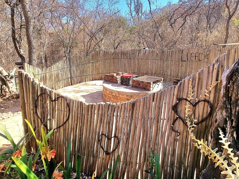 Outdoor entertainment area featuring a circular built-in brick braai enclosed by rustic reed fencing in a natural garden setting.