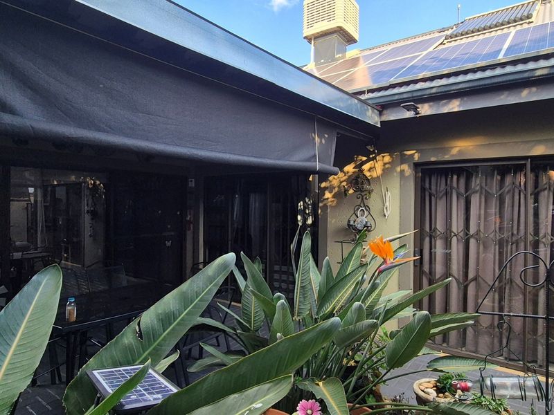 A covered outdoor patio area featuring a retractable awning, paved flooring, and direct access to the home through sliding glass doors with security gates.