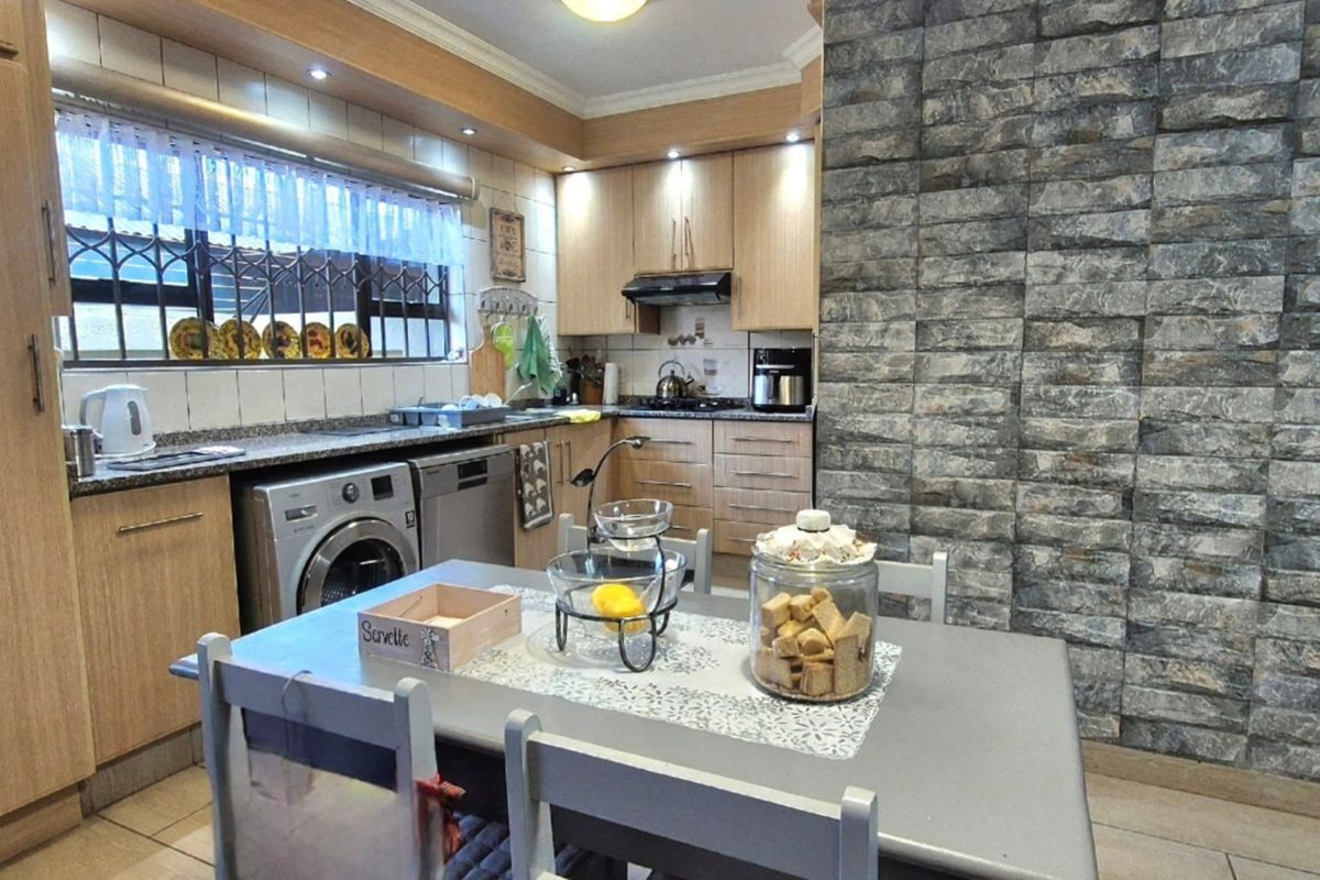 A functional kitchen featuring light wood cabinetry, granite countertops, a tiled backsplash, and a distinctive stone-cladding feature wall.