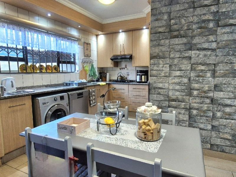 A functional kitchen featuring light wood cabinetry, granite countertops, a tiled backsplash, and a distinctive stone-cladding feature wall.