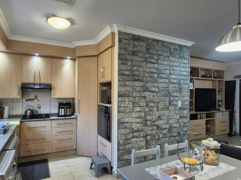 Open-plan kitchen and living area featuring light wood cabinetry, granite countertops, a stone-look feature wall, and integrated built-in shelving.