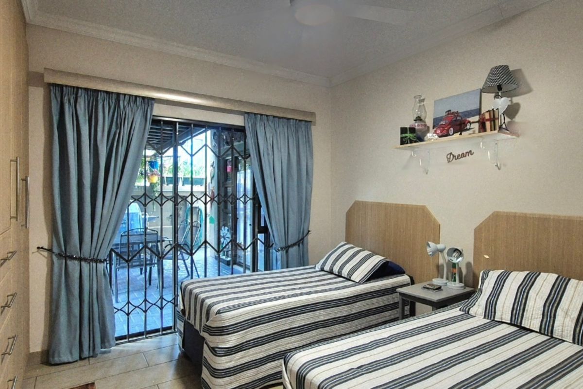 A functional bedroom featuring built-in wardrobes, tiled flooring, and a sliding door with security gate providing access to an outdoor patio area.