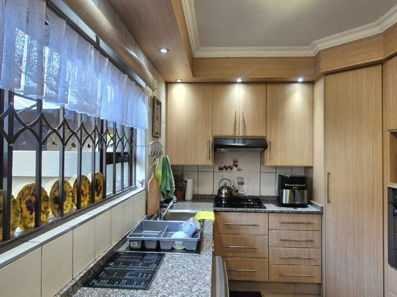 A functional kitchen featuring light wood cabinetry, granite countertops, a gas hob, built-in oven, and recessed lighting, with security bars on the window.