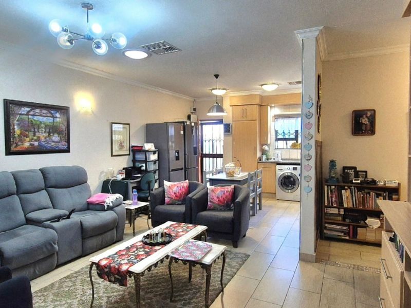 Open-plan living area featuring tiled flooring, integrated kitchen cabinetry, and a built-in shelving unit, creating a functional and connected living and dining space.