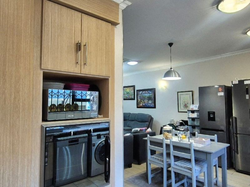 Open plan living and kitchen area featuring built-in cabinetry with integrated appliances, tiled flooring, and modern lighting fixtures.