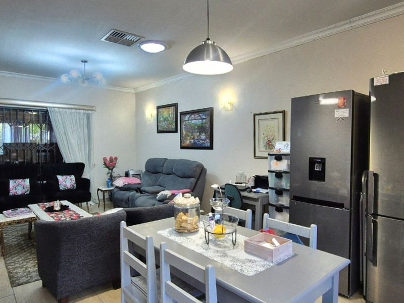 Spacious open-plan living and dining area featuring tiled flooring, recessed lighting, and direct access to an outdoor patio through a secure gate.