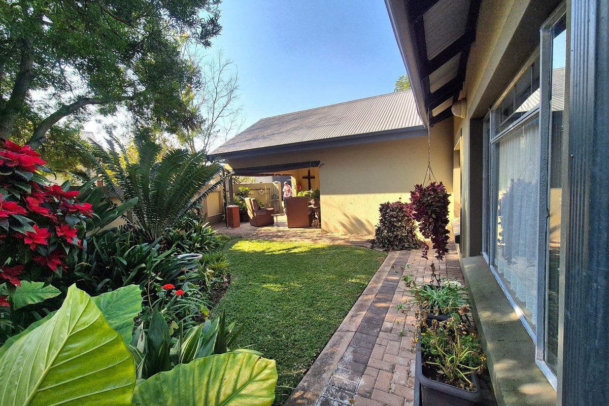 A well-maintained rear garden featuring a brick paved walkway, lush landscaping, and a covered patio area adjacent to the main house structure.