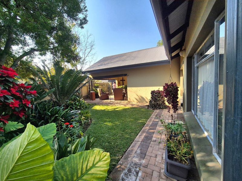 A well-maintained rear garden featuring a brick paved walkway, lush landscaping, and a covered patio area adjacent to the main house structure.