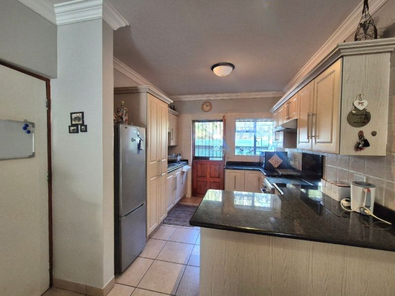 A functional kitchen featuring granite countertops, ample built-in cabinetry, tiled flooring, and direct access to the exterior via a security door.