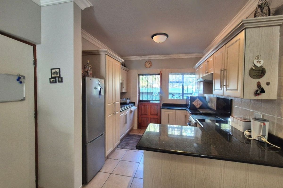 A functional kitchen featuring granite countertops, ample built-in cabinetry, tiled flooring, and direct access to the exterior via a security door.