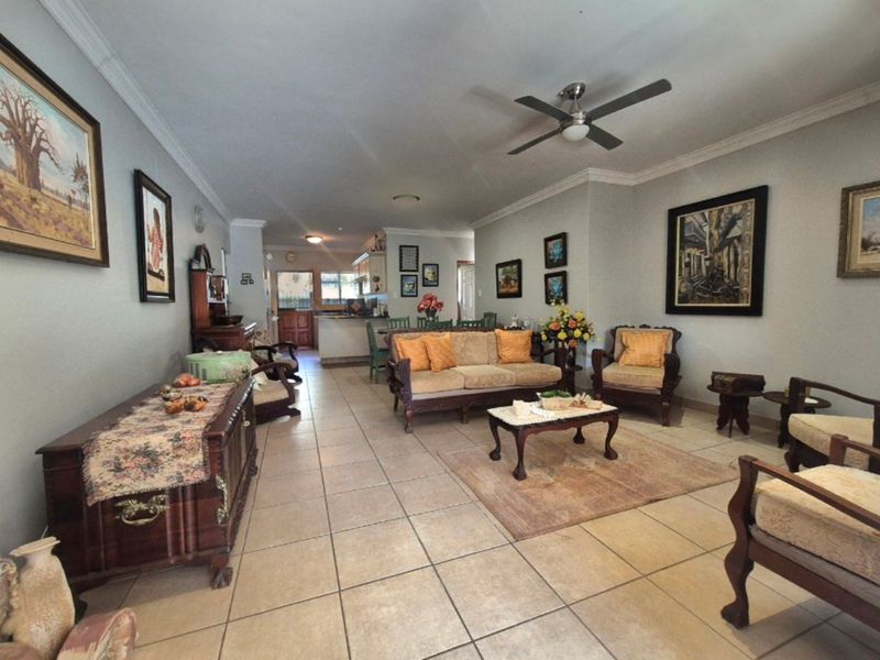 Spacious open-plan living area featuring tiled flooring, crown molding, and a ceiling fan, flowing seamlessly into the kitchen space.