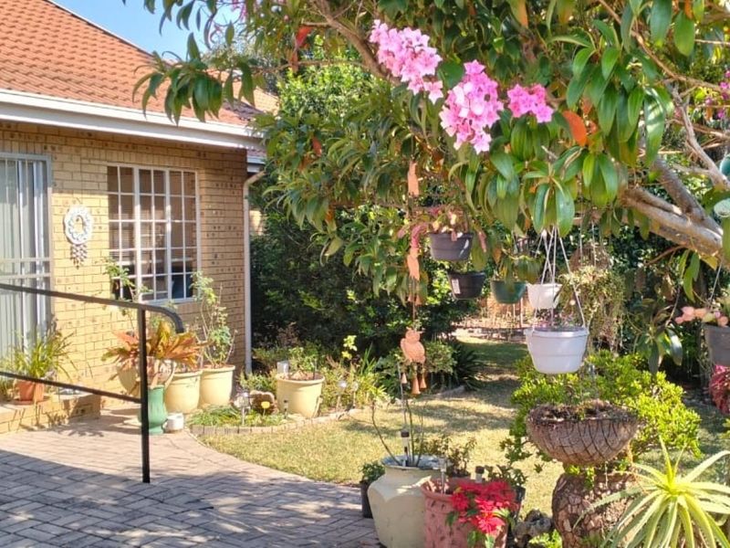 A view of the rear brick facade featuring a paved patio area, metal handrail, and a well-established garden with mature trees.