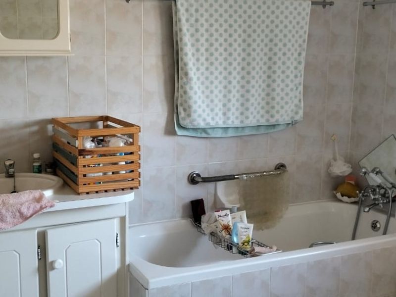 A dated bathroom featuring a built-in vanity with integrated sink, a standard bathtub with wall-mounted grab rail, and full-height wall tiling.