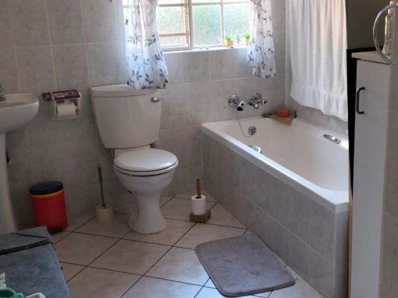 A functional bathroom featuring a pedestal basin, standard toilet, and a built-in bathtub with wall-to-wall tiling.