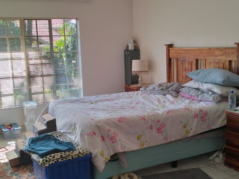 A functional bedroom featuring tiled flooring and large windows with venetian blinds, offering natural light and a view of the garden.