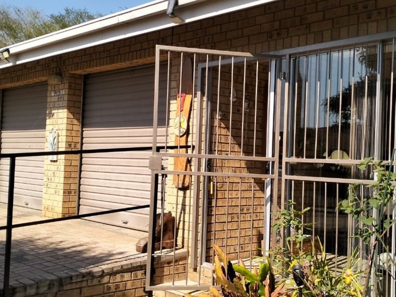 Front exterior view of the property featuring a brick facade, roller garage door, and secure metal entrance gate with paved driveway access.