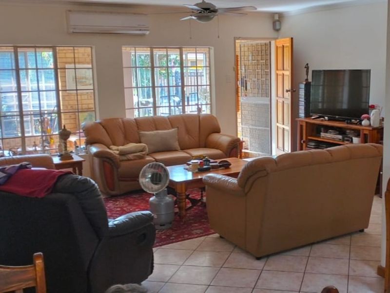 A spacious living room featuring tiled flooring, a ceiling fan, and a wall-mounted air conditioning unit, with direct access to the exterior.