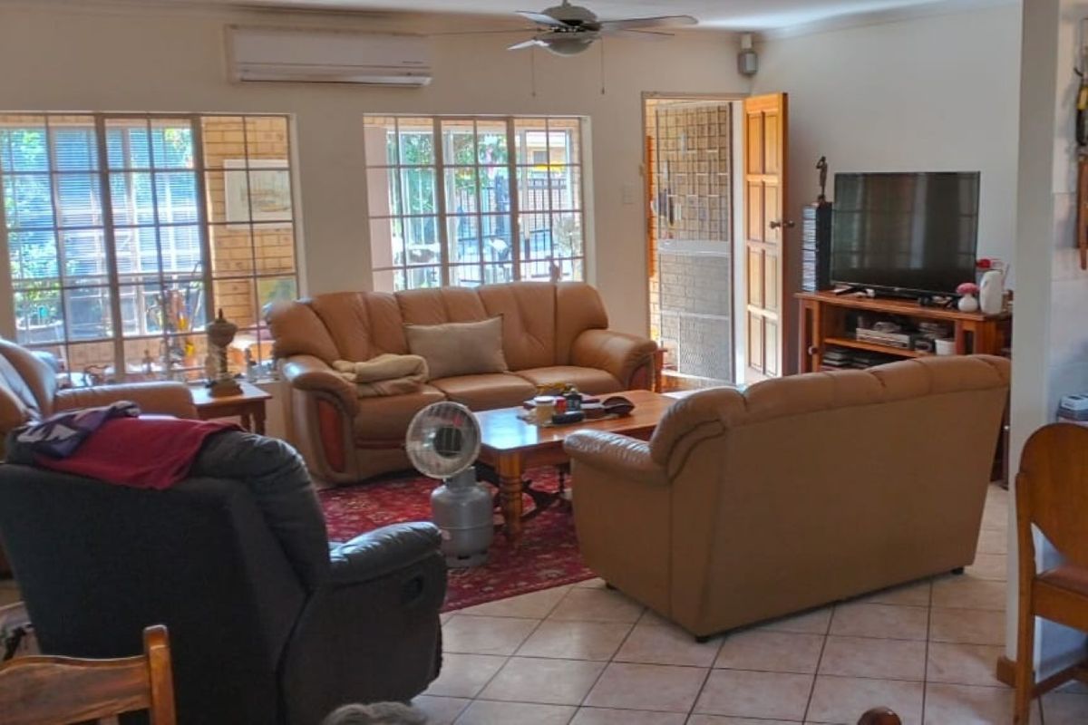 A spacious living room featuring tiled flooring, a ceiling fan, and a wall-mounted air conditioning unit, with direct access to the exterior.
