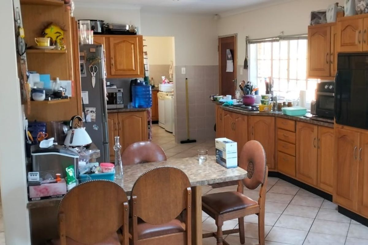 A functional kitchen featuring traditional wooden cabinetry, laminate countertops, and tiled flooring, with an open layout connecting to a secondary utility area.