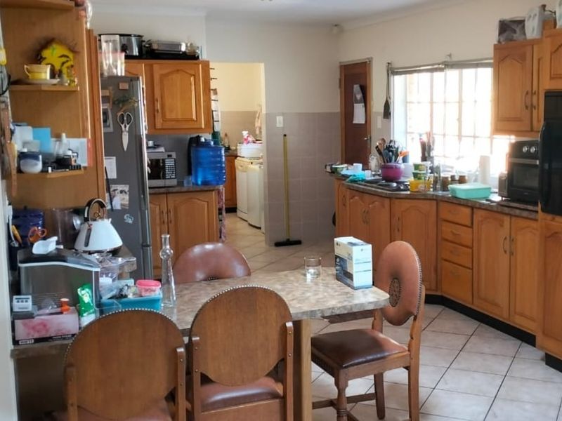 A functional kitchen featuring traditional wooden cabinetry, laminate countertops, and tiled flooring, with an open layout connecting to a secondary utility area.