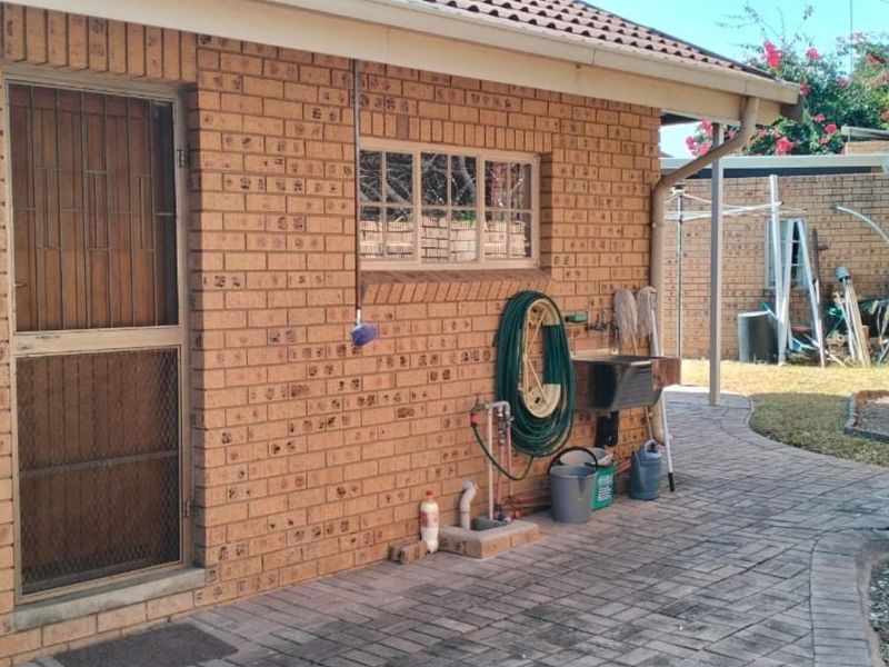 Rear exterior view of the property featuring face brick walls, a paved patio area, and a functional utility sink.