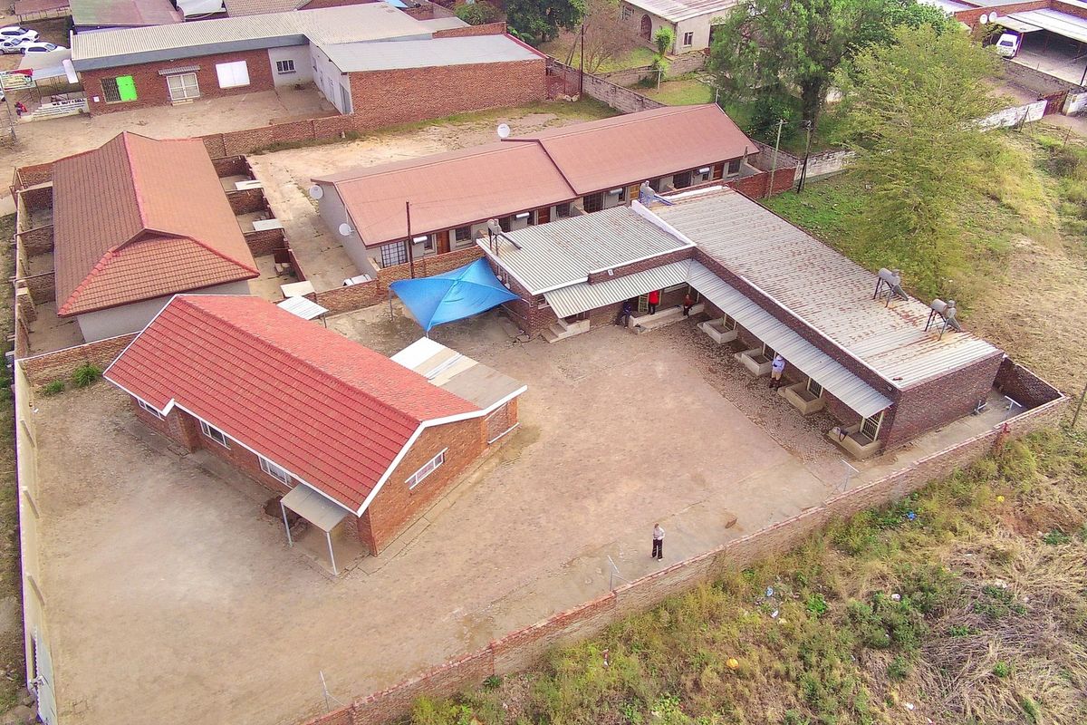 Aerial view of a property complex featuring multiple brick buildings with tiled and metal roofing, enclosed by a perimeter wall.