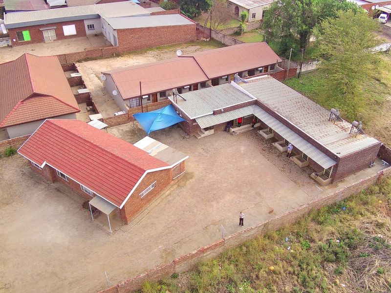 Aerial view of a property complex featuring multiple brick buildings with tiled and metal roofing, enclosed by a perimeter wall.