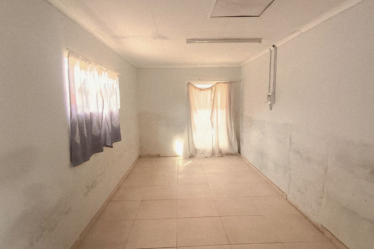 An empty, rectangular living area featuring tiled flooring and basic lighting, currently showing significant wall staining and requiring cosmetic updates.