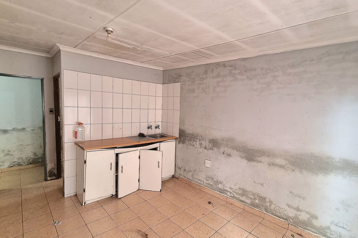 A small, empty kitchen area featuring tiled flooring, a basic sink unit, and significant wall dampness requiring repair and renovation.