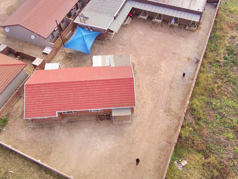 Aerial view of a property featuring multiple buildings with tiled roofs, a large paved courtyard, and a perimeter boundary wall.