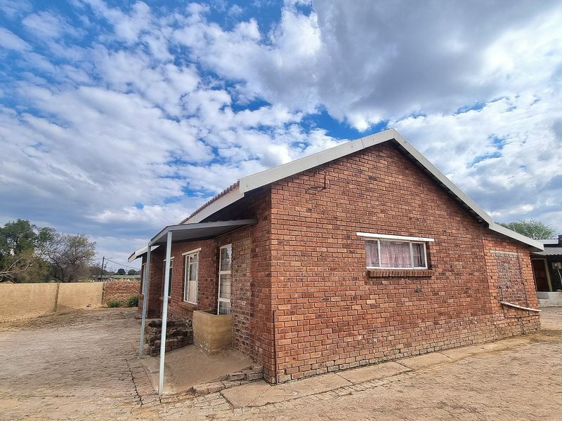 Rear view of a brick house featuring a paved yard, perimeter wall, and a small covered patio area.