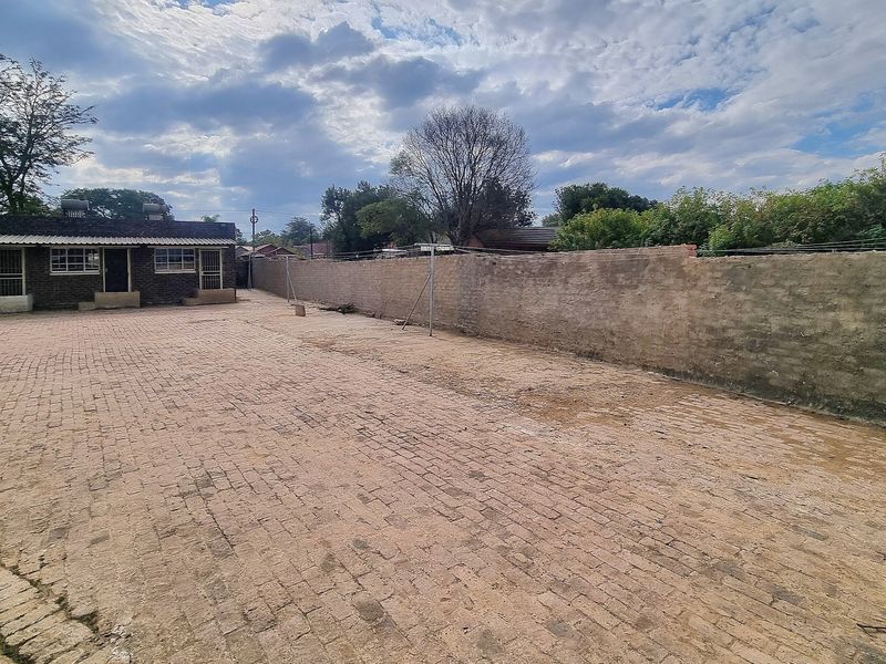 A spacious rear exterior area featuring extensive brick paving and a long perimeter boundary wall, providing a functional outdoor space.