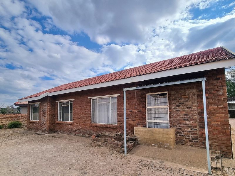 Rear view of a face brick house featuring a tiled roof, steel windows, and a paved driveway area.
