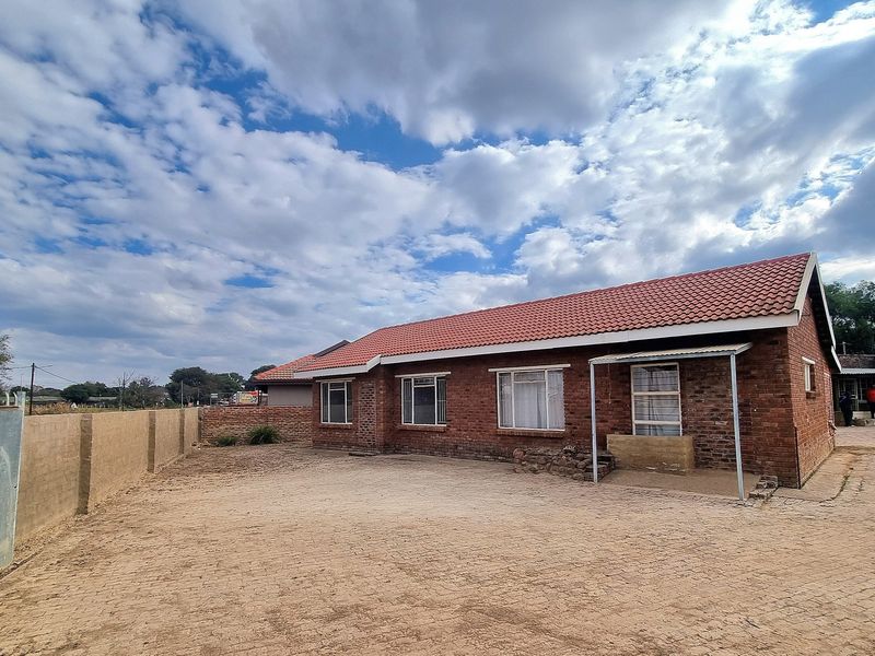 A single-story brick house featuring a tiled roof, a paved driveway, and a perimeter wall, set on a spacious plot.