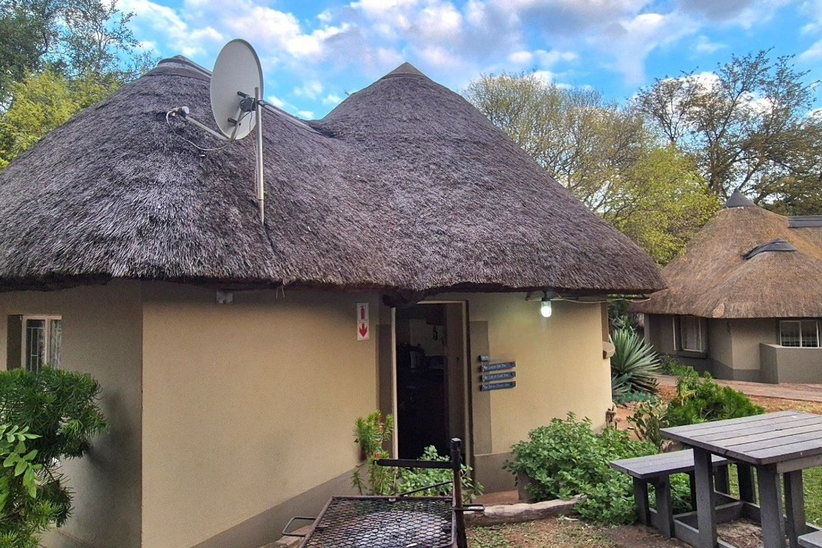 Exterior view of a traditional thatched-roof cottage featuring a satellite dish and outdoor lighting, set within a landscaped garden area.