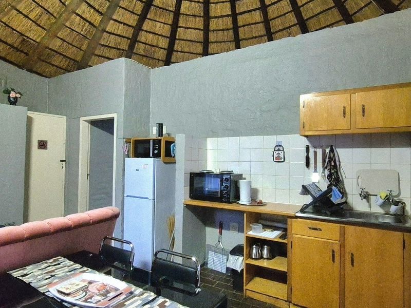 Open plan kitchen area featuring a traditional thatched roof, exposed rafters, and timber cabinetry with a tiled backsplash.