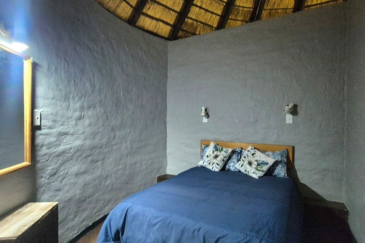 A rustic bedroom featuring a traditional thatched roof with exposed rafters and textured grey walls, providing a unique, character-filled living space.