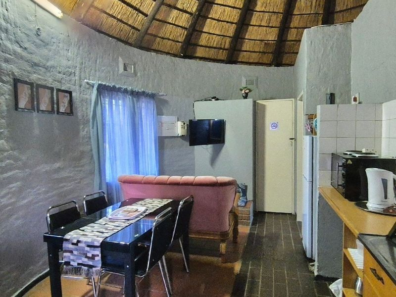 Open-plan living and kitchen area featuring a traditional thatched roof, textured stone walls, and functional built-in cabinetry.