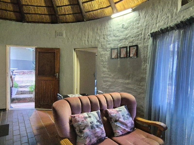 Open plan living area featuring a unique thatched roof, exposed brick walls, and integrated kitchen cabinetry with direct access to the exterior.