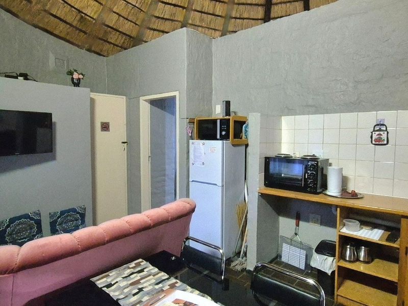 Open-plan living area featuring a rustic thatched roof, compact kitchen with wooden cabinetry, and tiled backsplash in a functional layout.