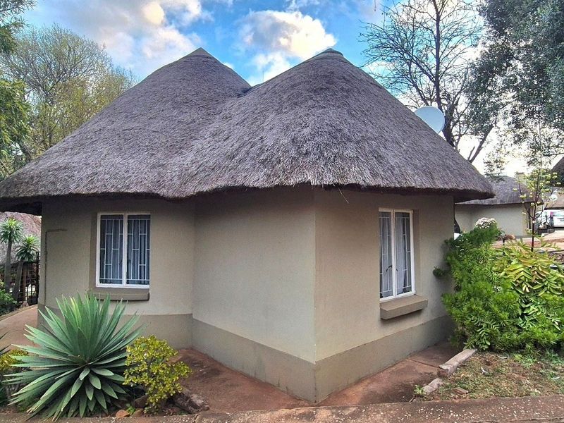 A charming detached cottage featuring a traditional thatch roof, plastered exterior walls, and secure casement windows set within a landscaped garden environment.