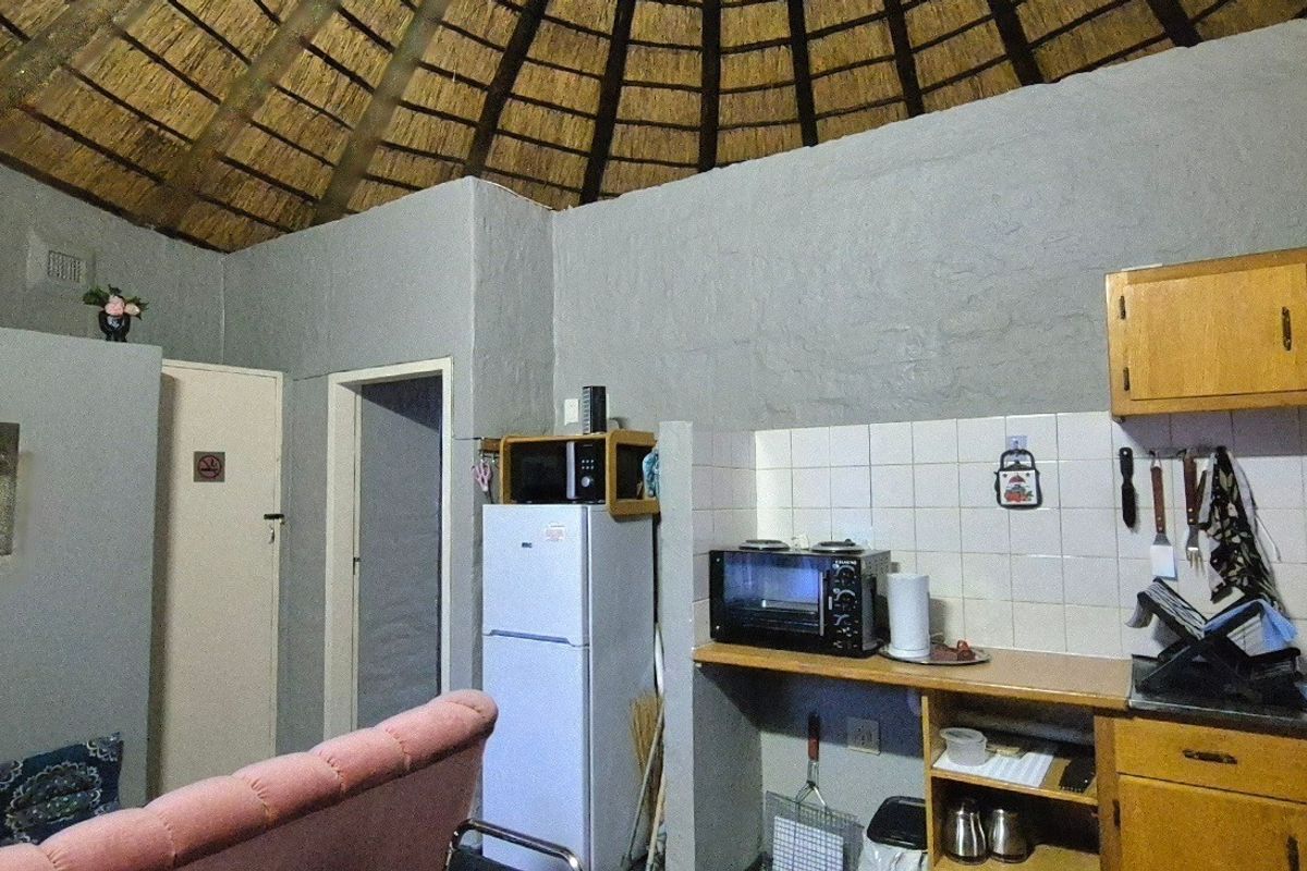 A compact kitchen area featuring wooden cabinetry, tiled backsplash, and a unique exposed thatched roof ceiling within a rustic circular room structure.