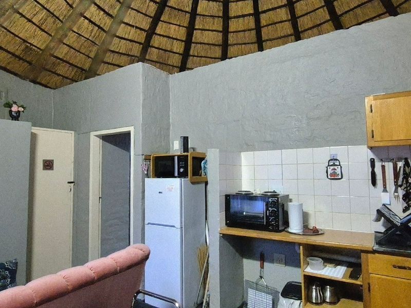A compact kitchen area featuring wooden cabinetry, tiled backsplash, and a unique exposed thatched roof ceiling within a rustic circular room structure.